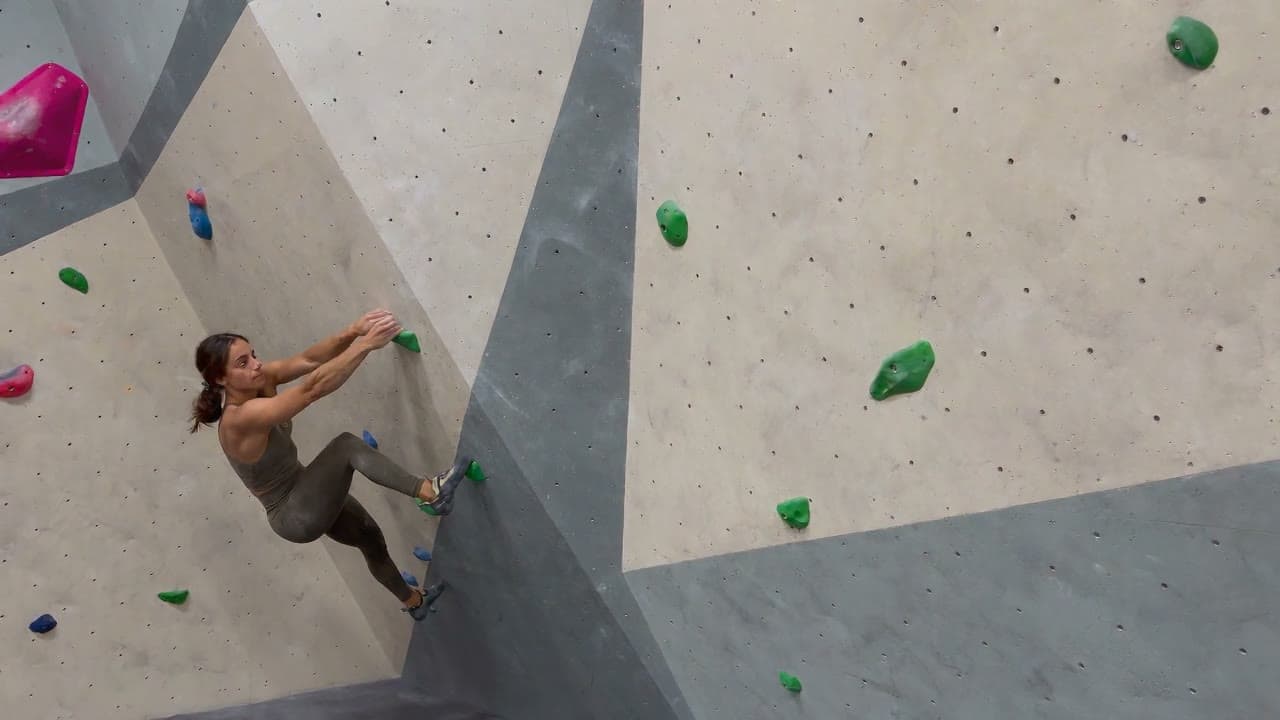 A woman climbing a bouldering wall, then high-fiving the camera